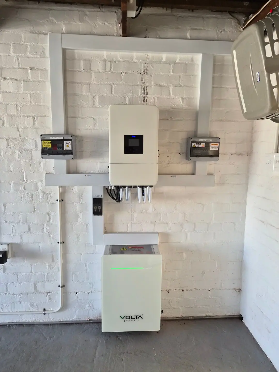 A hybrid inverter, PV string board, AC transfer board and lithium battery installed on a white brick wall with neat trunking